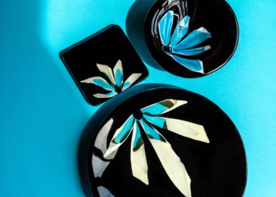 ensemble d'assiettes de verre noir avec pétales illustrant des demi fleurs aux couleurs lumineuses de blanc, crème et turquoise.