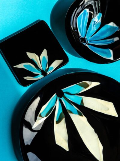 ensemble d'assiettes de verre noir avec pétales illustrant des demi fleurs aux couleurs lumineuses de blanc, crème et turquoise.