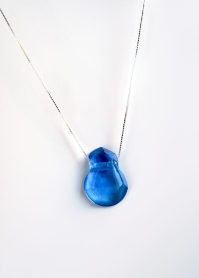 Pendentif en cristal de verre turquoise, facetté à la main, suspendu à une chaîne fine en argent sterling de 18 pouces. Son bleu éclatant évoque les eaux limpides d’un lagon, jouant avec la lumière à chaque mouvement.