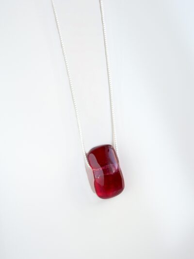 Pendentif en cristal de verre rouge framboise, légèrement arrondi et translucide, suspendu à une chaîne fine en argent