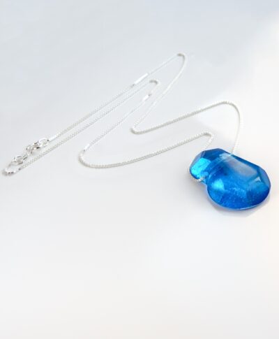 Pendentif en cristal de verre turquoise, facetté à la main, suspendu à une chaîne fine en argent sterling de 18 pouces. Son bleu éclatant capte la lumière et révèle des nuances vives et cristallines.