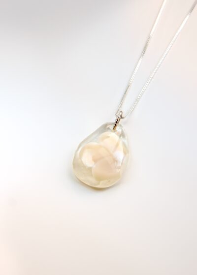 Pendentif en verre transparent en forme de goutte, avec un motif de fleur blanche délicatement incrusté, suspendu à une chaîne en argent.