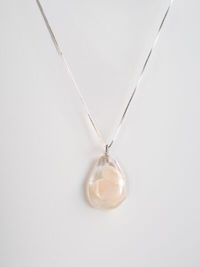 Pendentif en verre transparent en forme de goutte, avec un motif de fleur blanche délicatement incrusté, suspendu à une chaîne en argent.