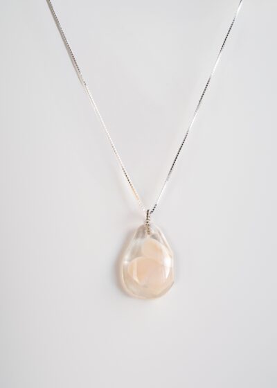 Pendentif en verre transparent en forme de goutte, avec un motif de fleur blanche délicatement incrusté, suspendu à une chaîne en argent.