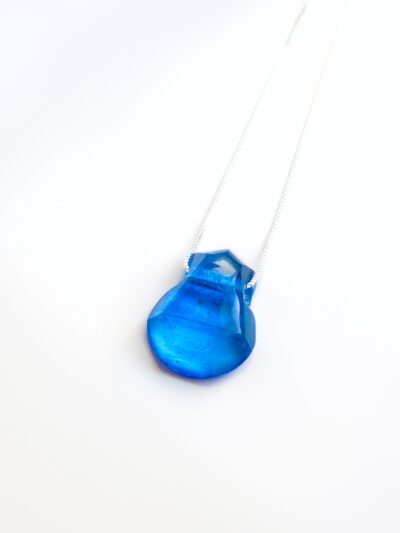 Pendentif en cristal de verre turquoise, facetté à la main, suspendu à une chaîne fine en argent sterling de 18 pouces. Son bleu éclatant capte la lumière et révèle des nuances vives et cristallines.